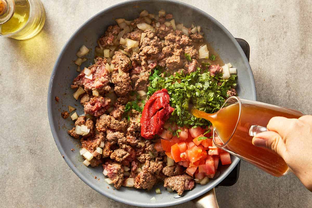 Top overview of beef stock being pour into a pan with beef for sweet potato brownies