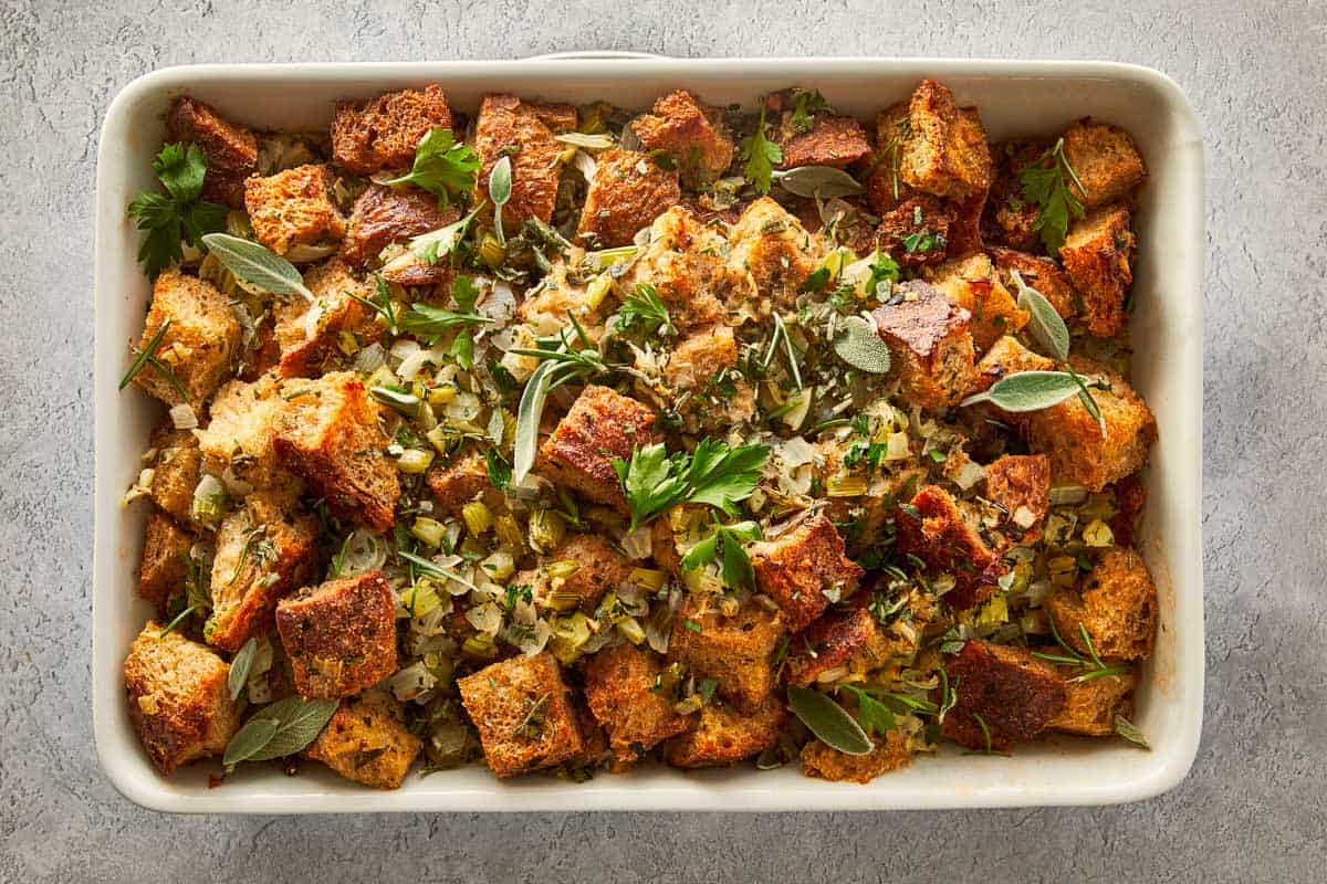 Baked buttery herb stuffing in a white casserole dish, garnished with fresh sage and parsley, a good holiday side dish.
