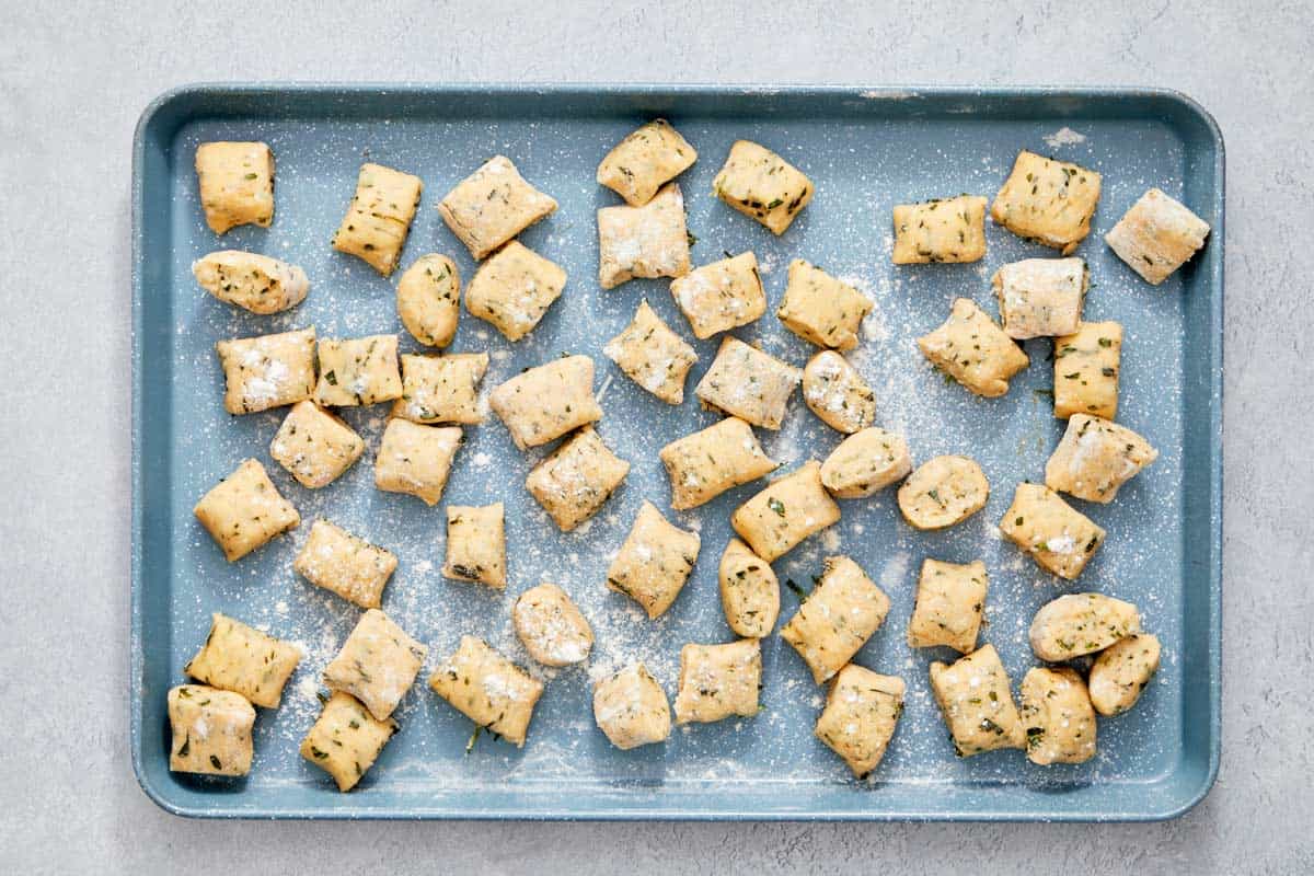 Uncooked gnocchi pieces on a floured baking tray.