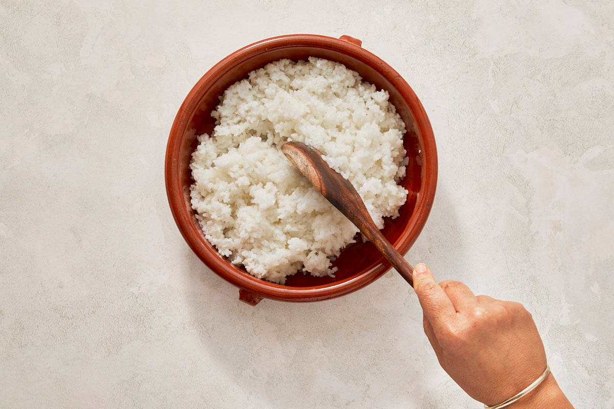 Hand grips a wooden spoon, poised over a bowl of rice