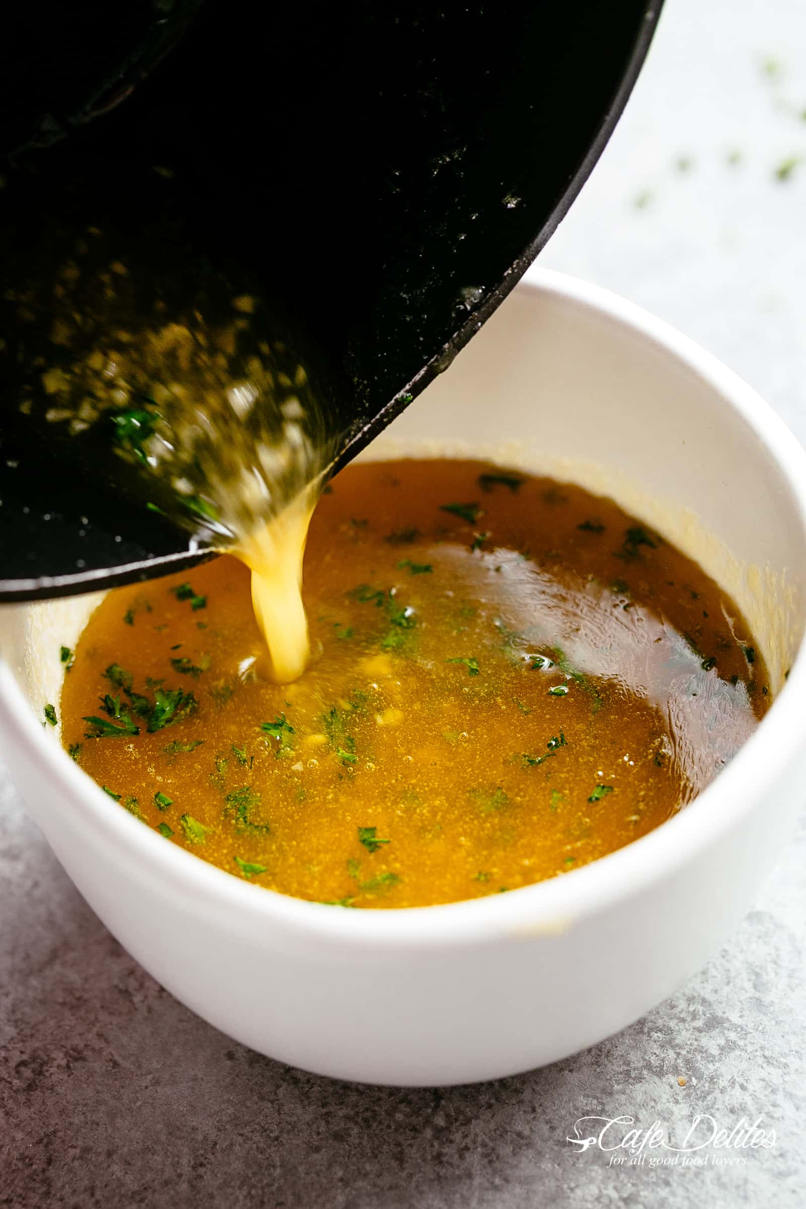 Hot & Spicy Golden Honey Garlic Butter Sauce pouring from a black pot into small white sauce cup with small bits of garlic and parsley.