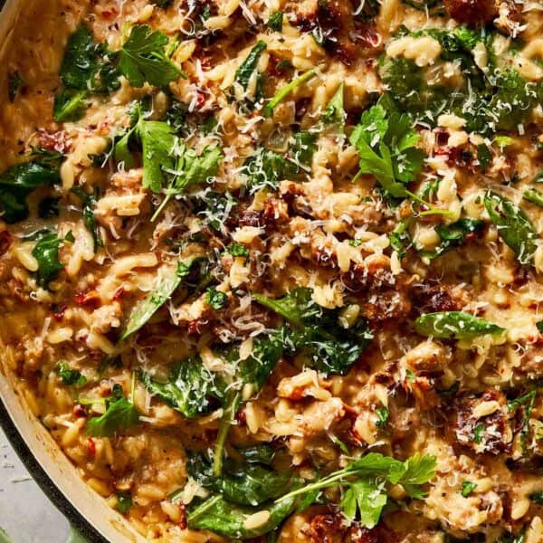 Close-up of creamy Italian sausage and spinach orzo in a skillet, garnished with Parmesan and parsley.