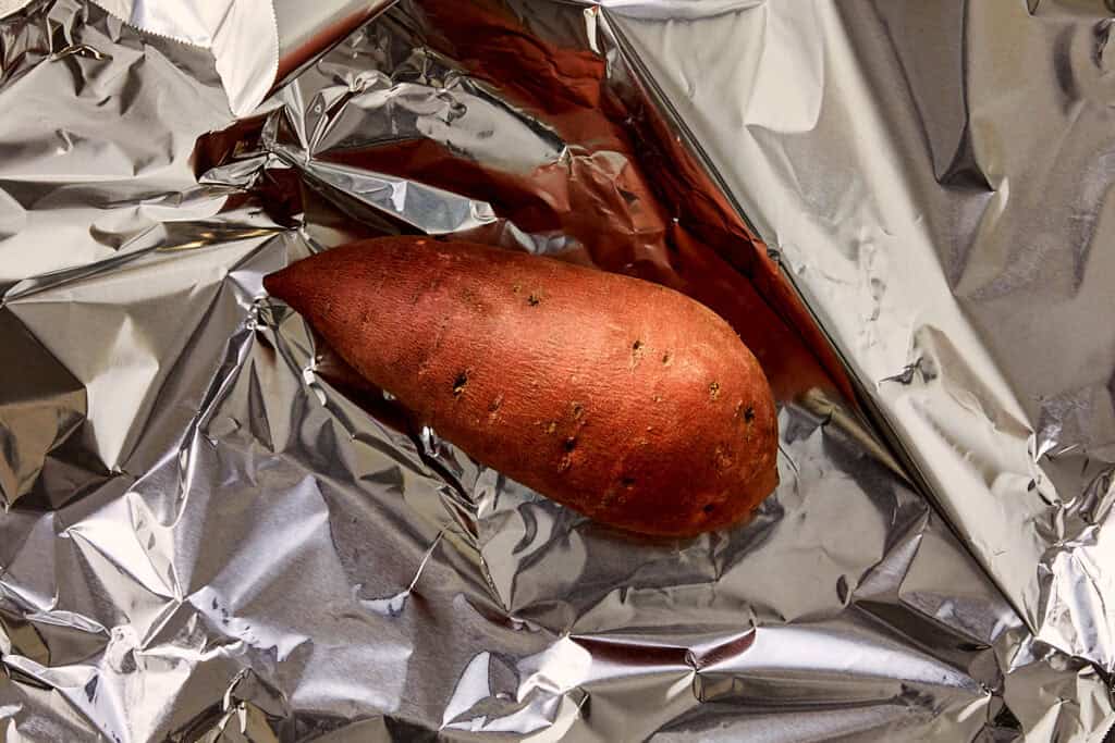 Whole sweet potato wrapped in foil, unpeeled and ready to roast in the oven.