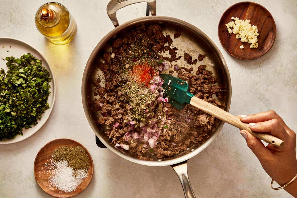 Adding seasoning and chopped onions to browned beef.
