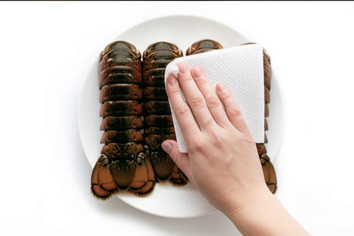 Hand with paper towel and lobster tails.