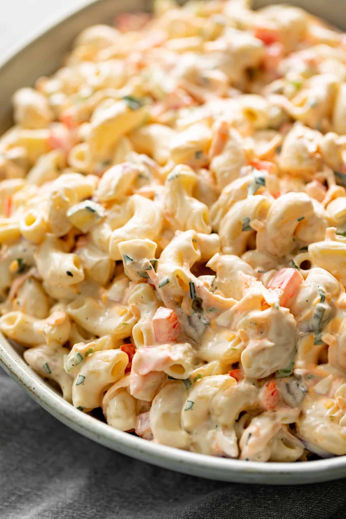 With a good creamy mayo dressing and fresh ingredients, A super creamy macaroni salad is so easy and quick to make! You\'ll love this recipe! Served in a light grey bowl on a grey linen cloth.