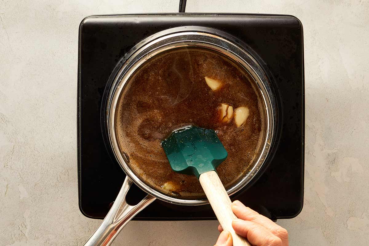 A person using a spatula to mix soup in a pot, while preparing glaze for the ham.