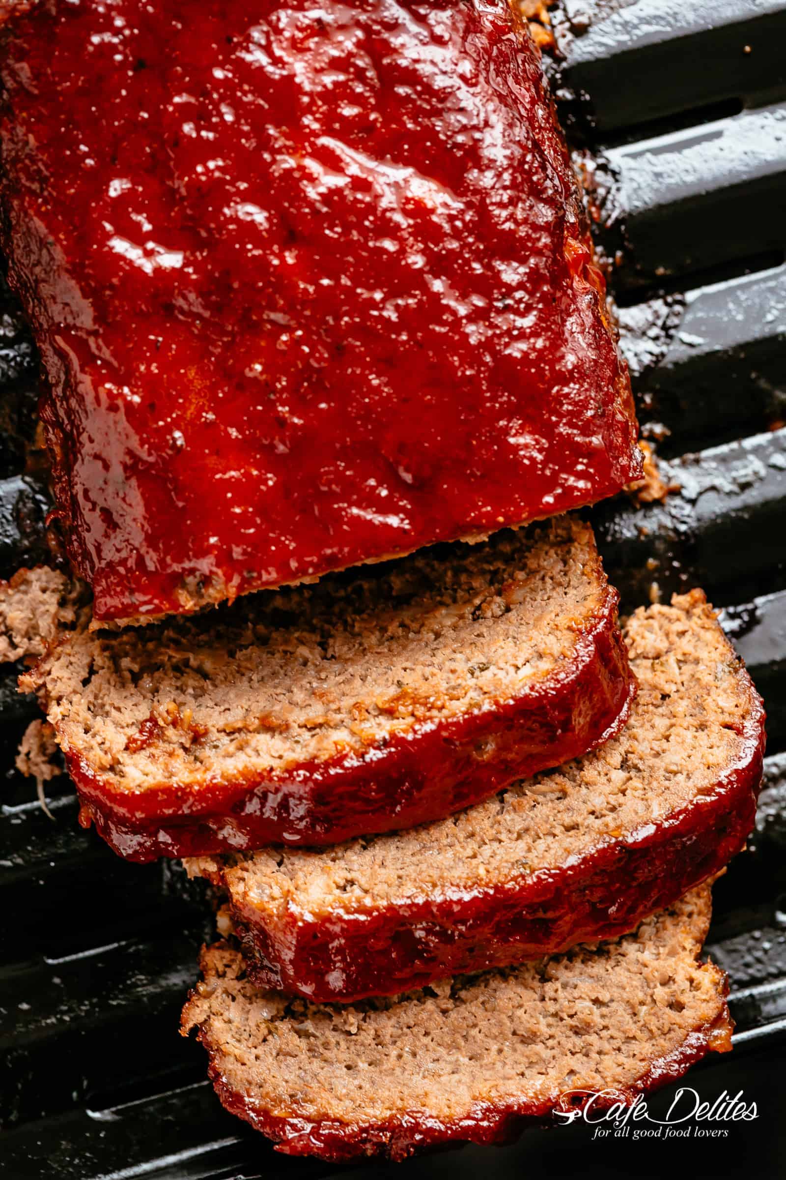 Bird's eye view of grilled meatloaf on a grill, with three slices cut off the end.
