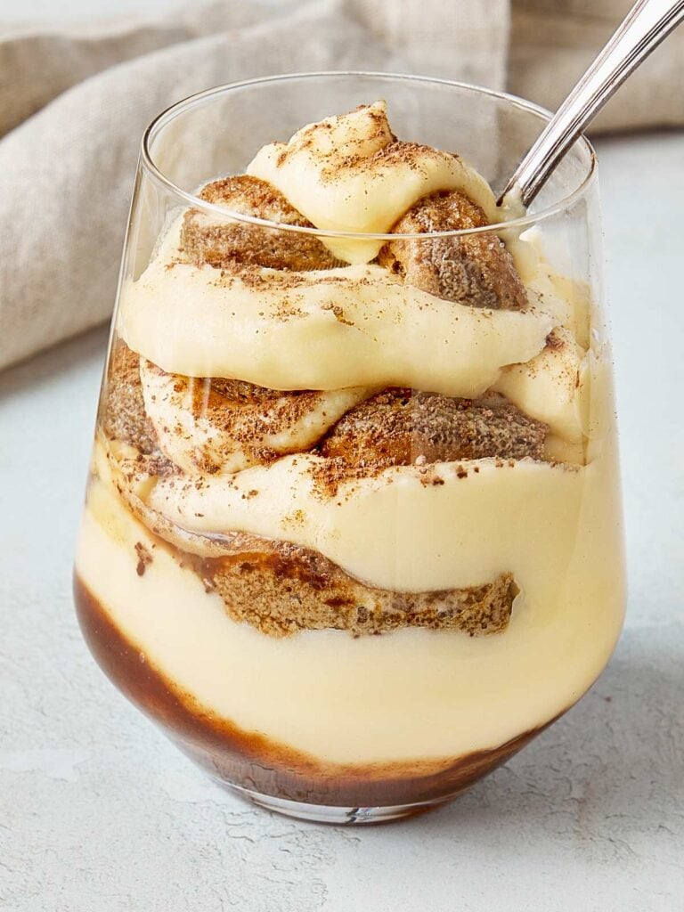 Single serving of tiramisu in a glass, layered with creamy mascarpone and espresso-soaked ladyfingers, topped with cocoa powder.