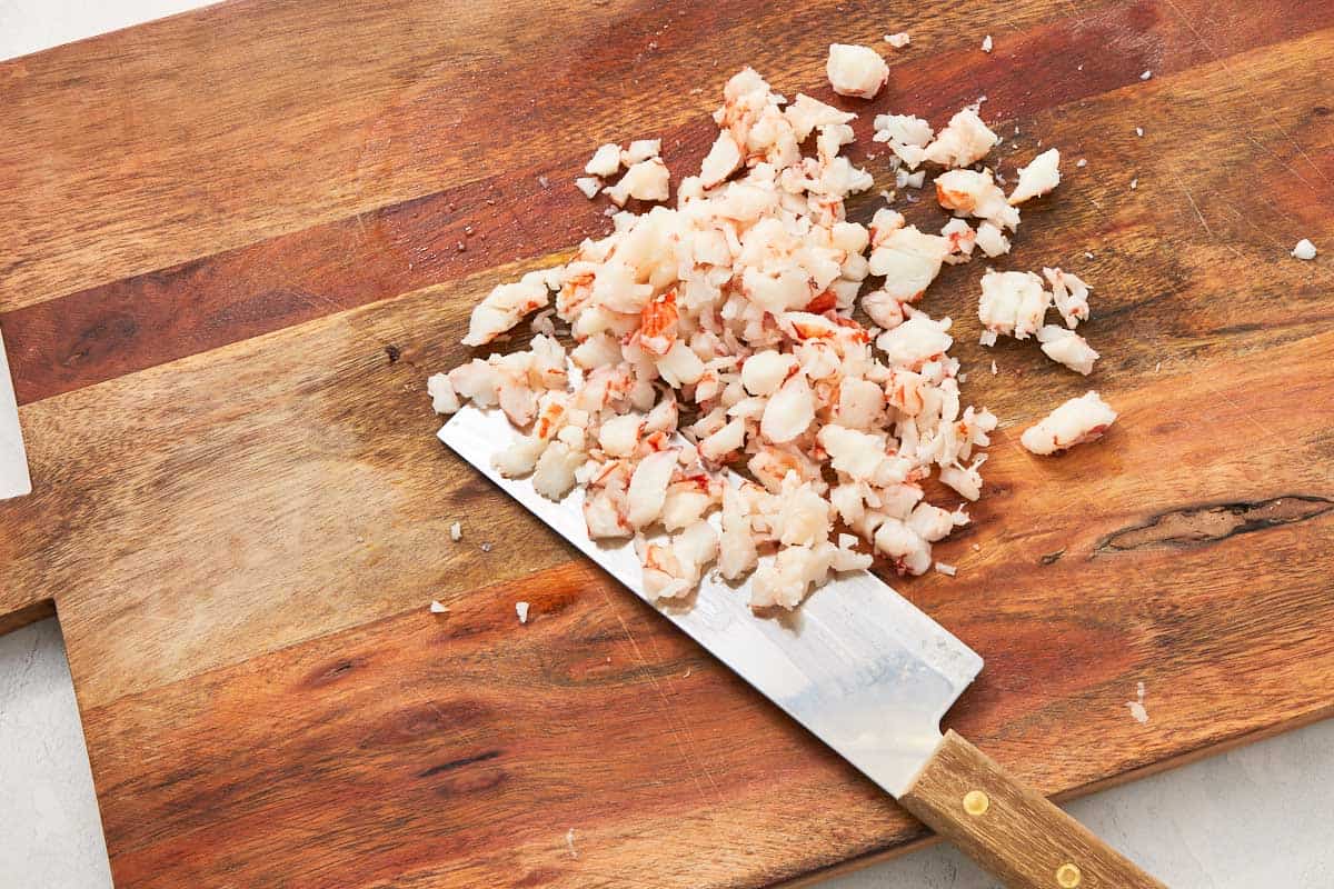Chopped cooked shrimp on a wooden cutting board with a chef's knife.