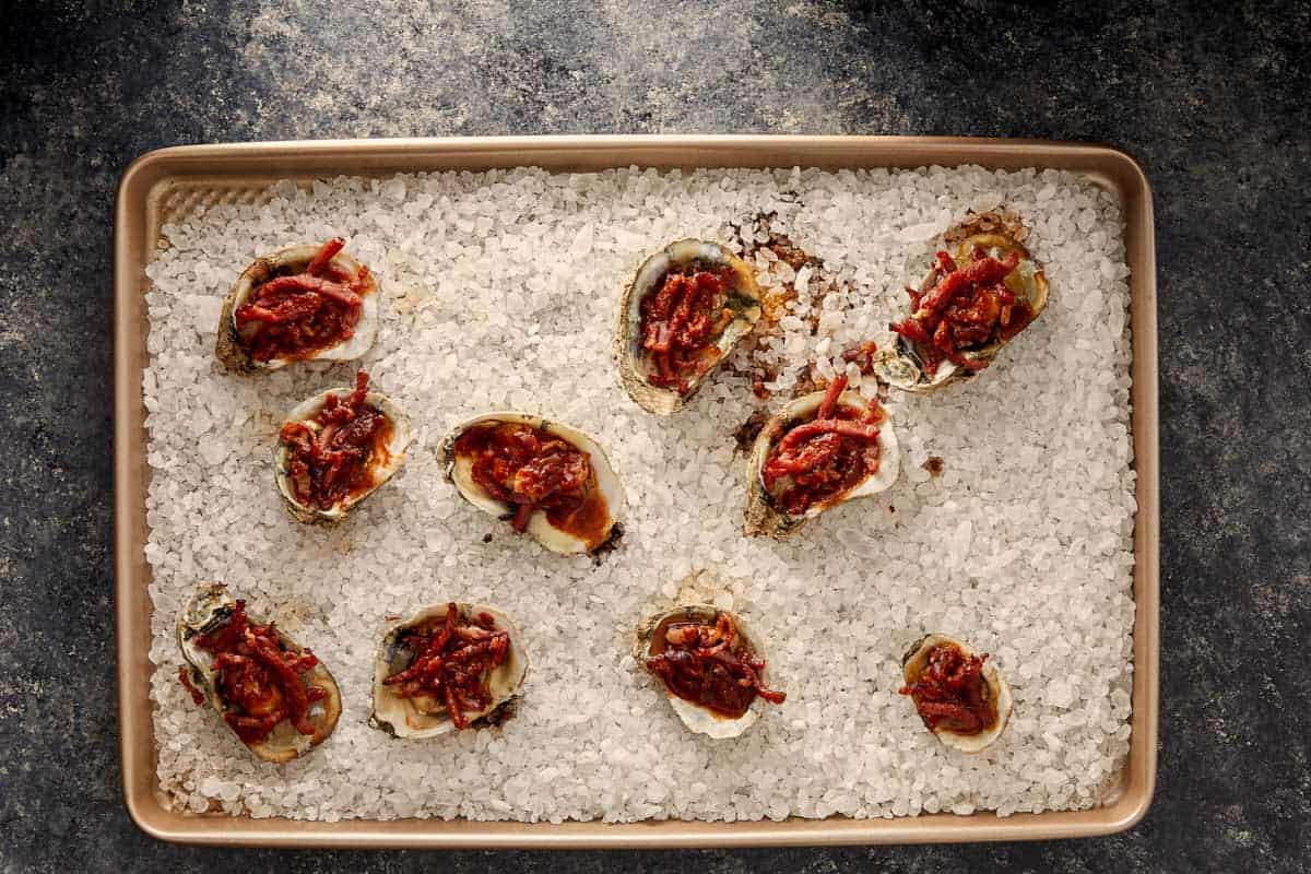 Baked oysters topped with bacon and sauce on a tray of rock salt.
