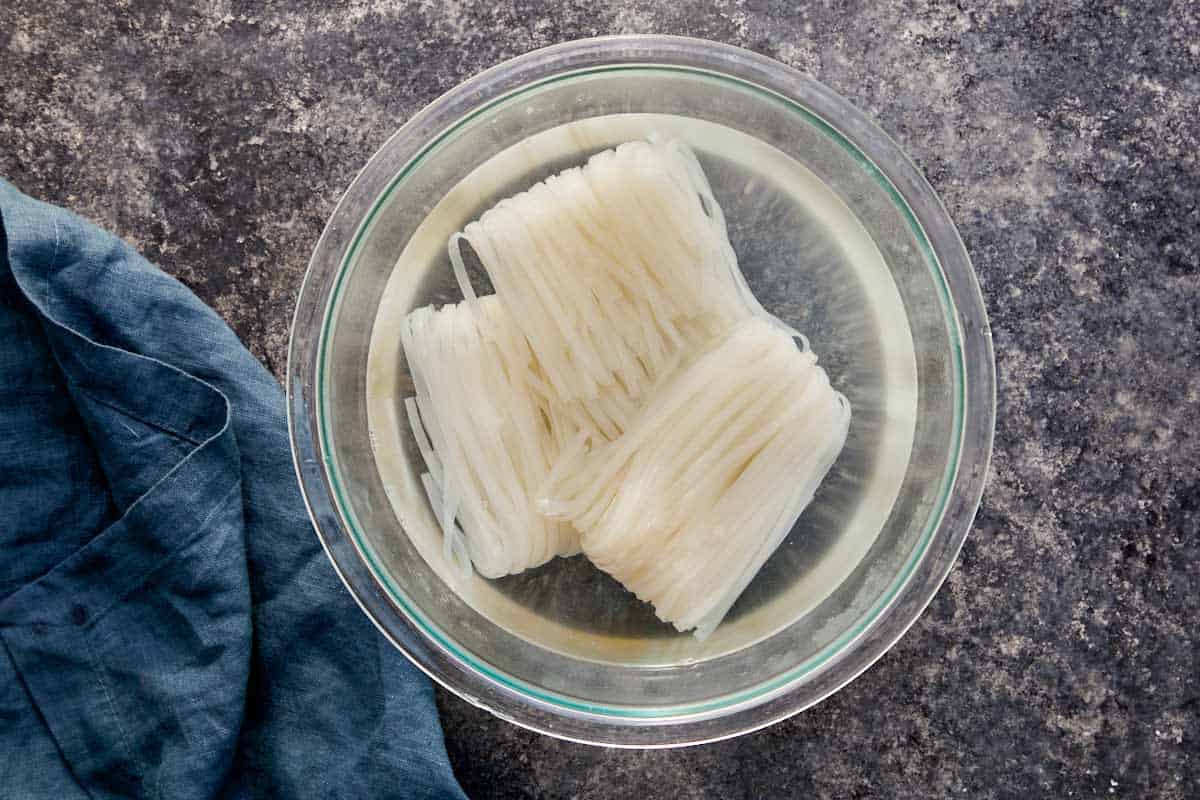 Rice noodles soaking in a glass bowl of water.