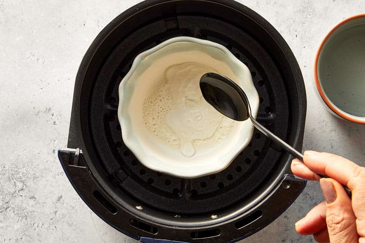 Top overview of a hand pouring 2 tbsp of water in a ramekin