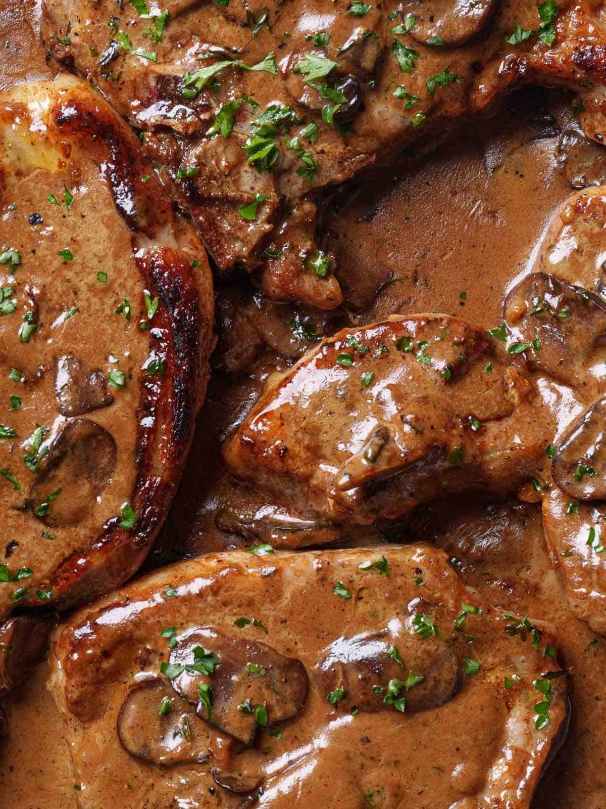 Golden-brown seared pork chops nestled in a pan of creamy garlic mushroom sauce.