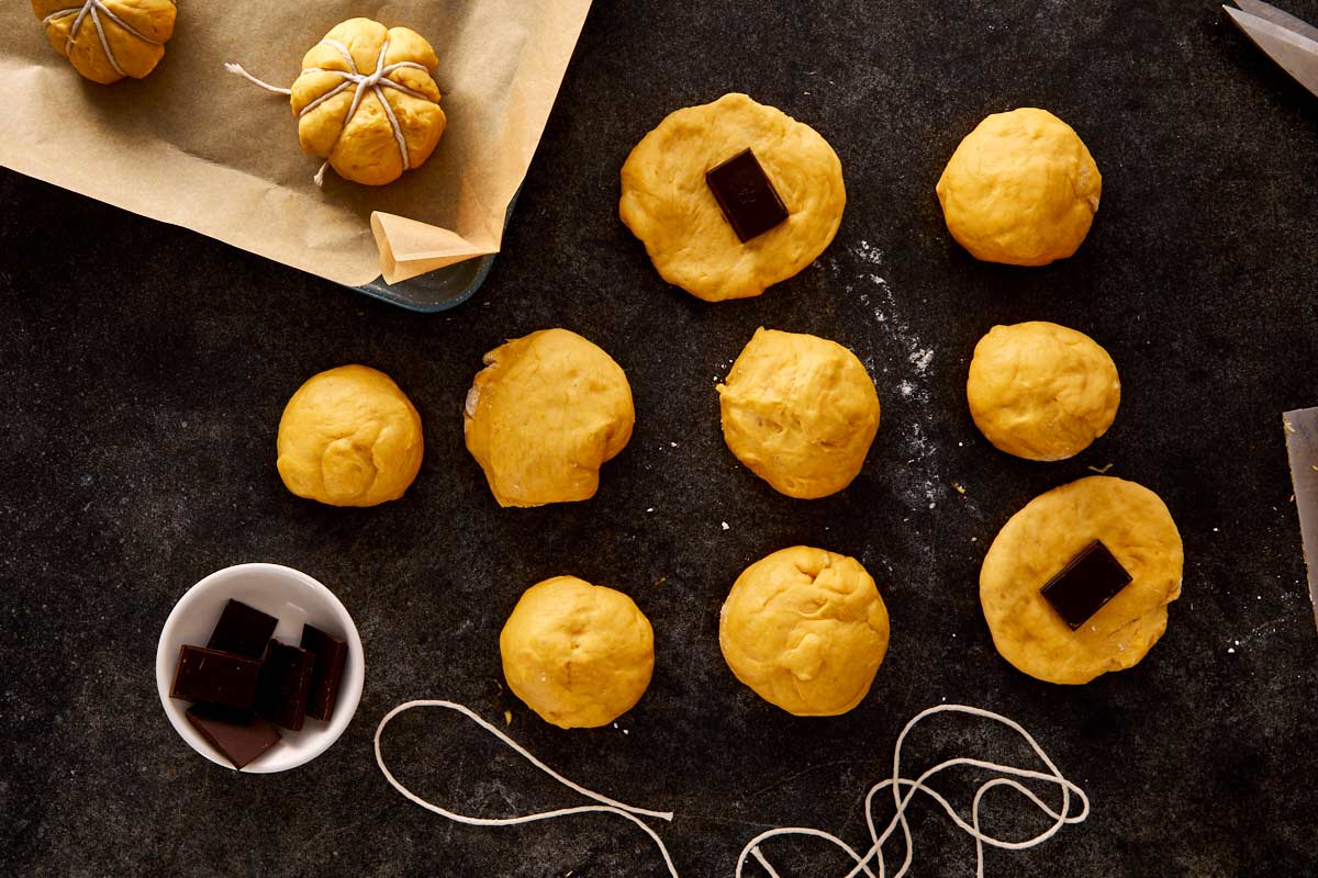 Pumpkin bread dough divided into portions with chocolate squares placed in the center, ready to be shaped.