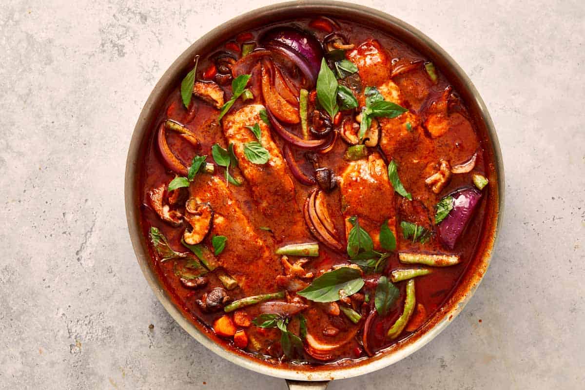 Final simmer of Salmon Panang Curry, a vibrant red sauce filled with salmon, basil, and colorful vegetables ready to serve.