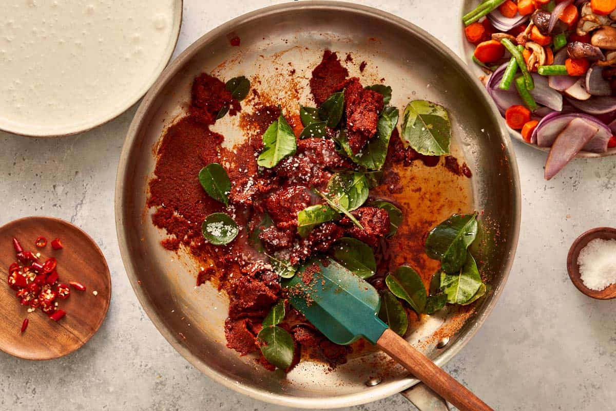 Panang curry paste and kaffir lime leaves sizzling in oil, releasing rich Thai aromas as the curry base starts to come together.