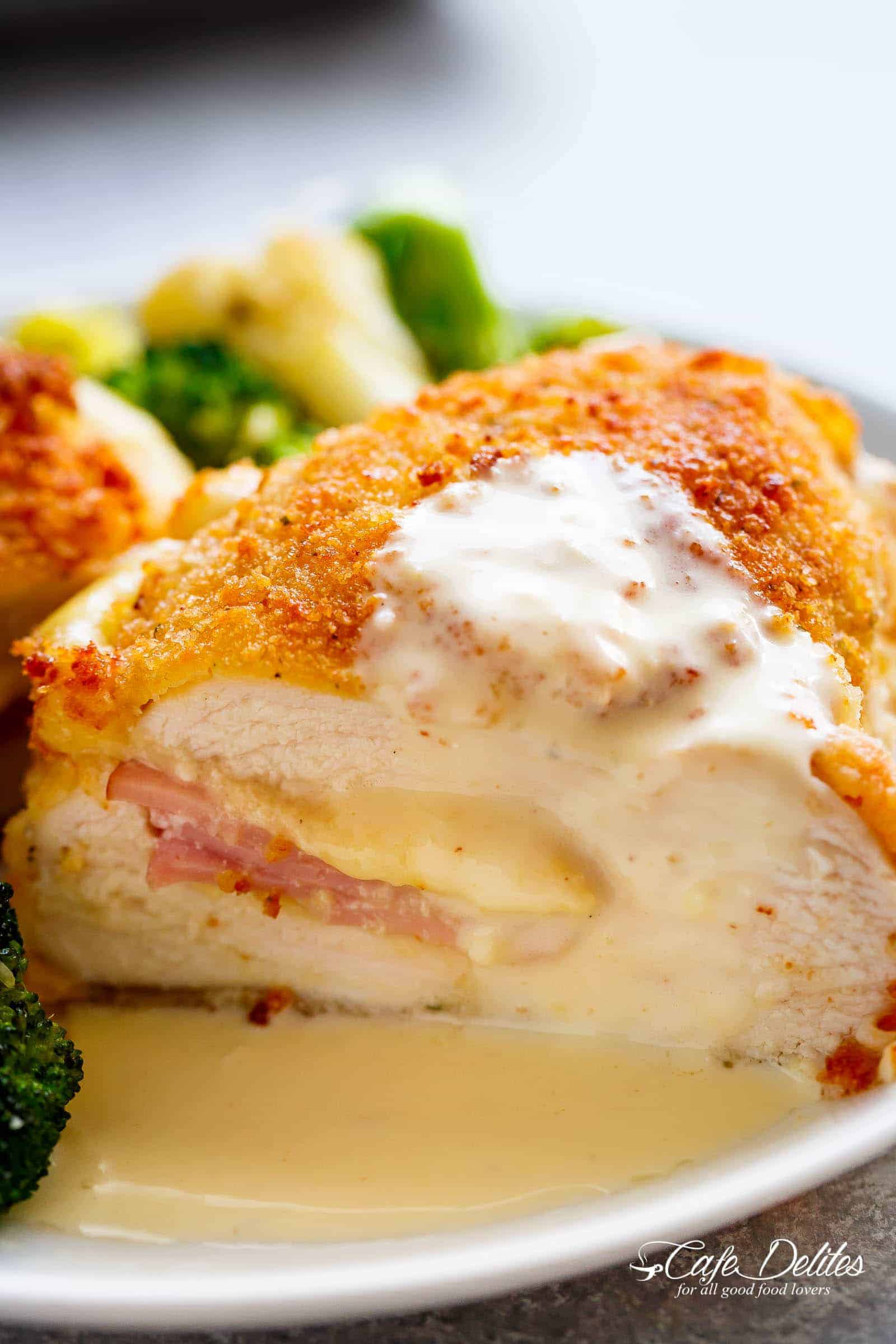 Side view of Crispy crumbed chicken breasts filled with Dijon mustard, Swiss cheese and ham, baked with vegetables and served with an good Dijon Cream Sauce