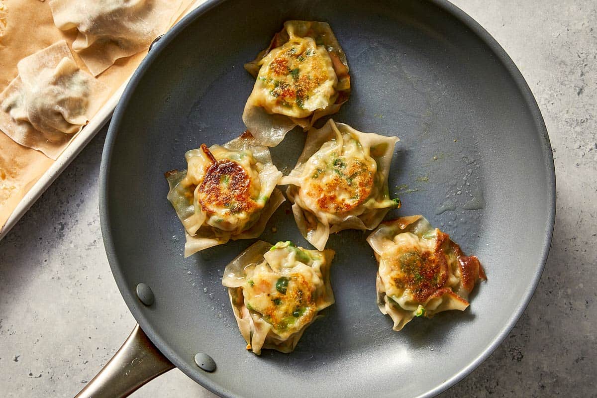 Pan-fried shrimp dumplings in a skillet, flipped over to reveal their crispy, browned crust after the water has evaporated.