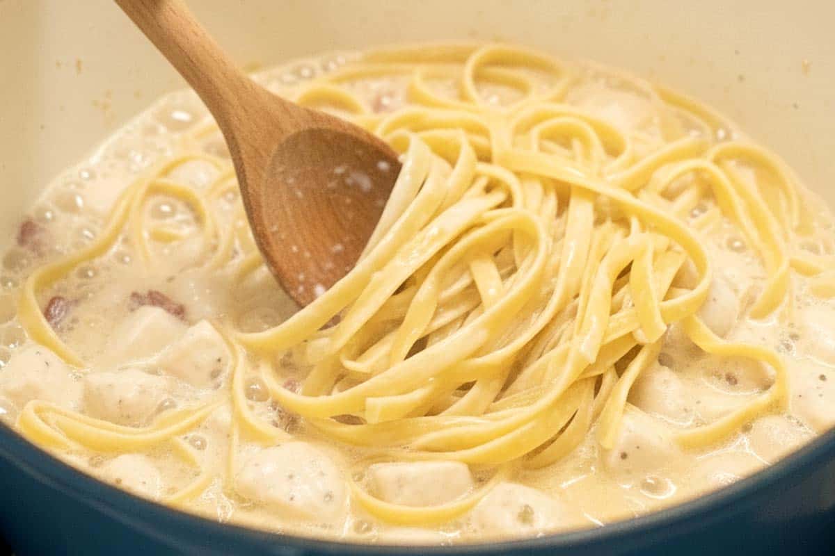 Stirring the pasta using a wooden spoon.
