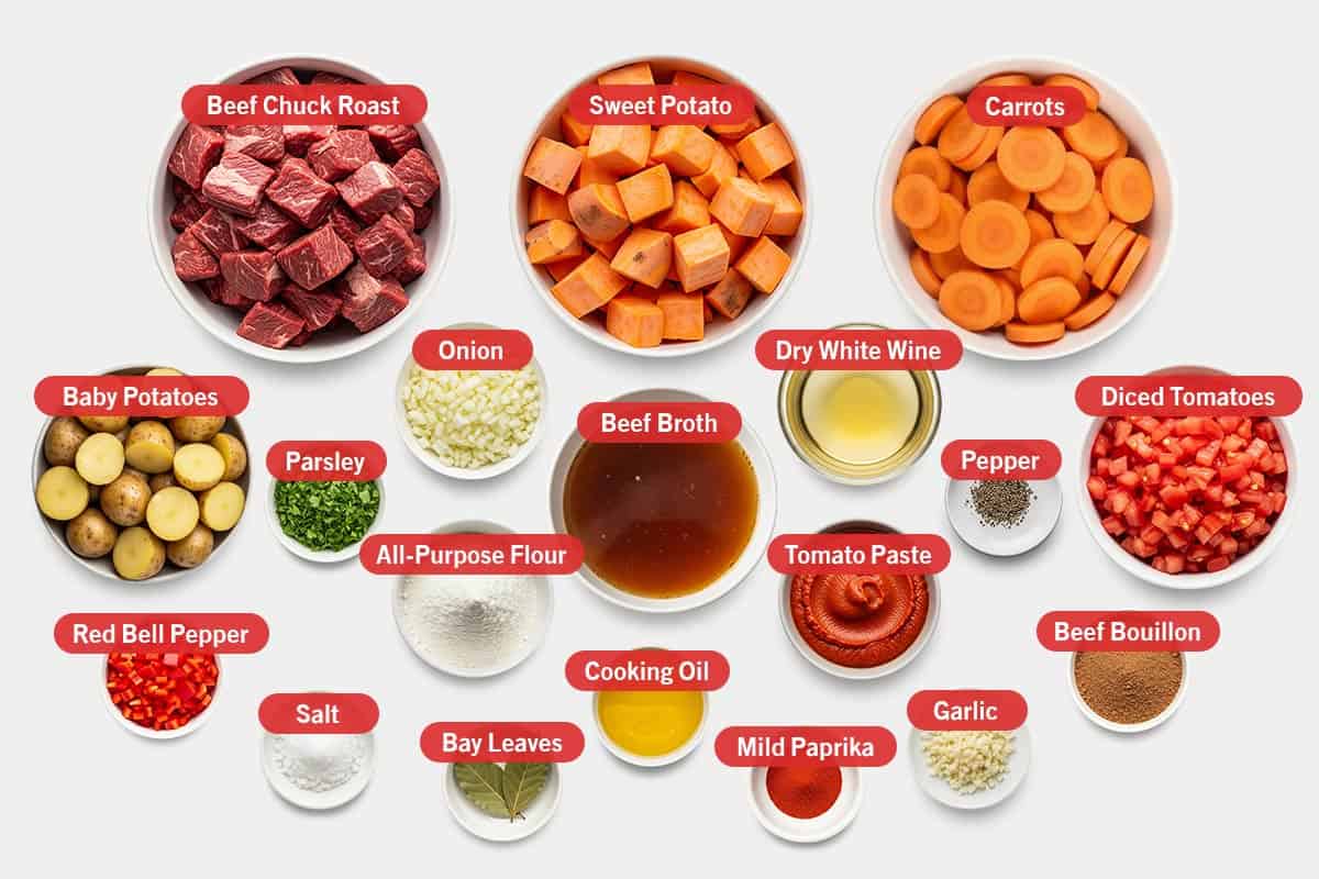 Top shot of ingredients: Beef chuck roast, sweet potato, carrots, baby potatoes, parsley, onion, beef broth, dry white wine, pepper, diced tomatoes, beef bouillon, tomato paste, all-purpose flour, red bell pepper, salt, bay leaves, cooking oil, mild paprika, and garlic.