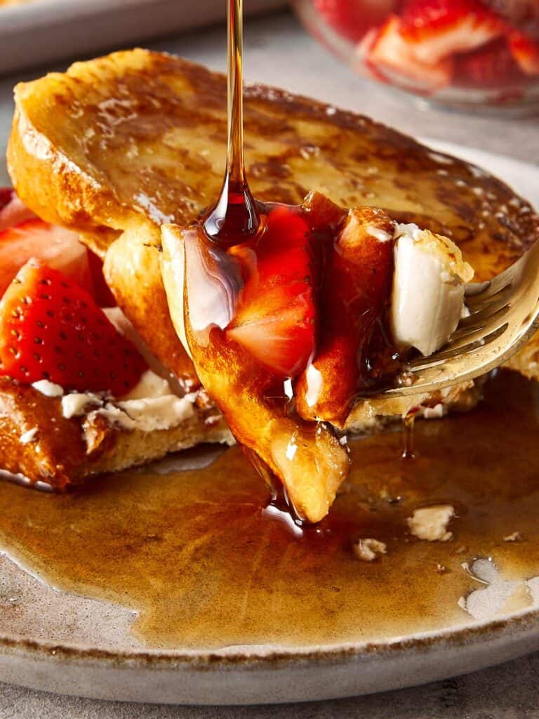 close up of brioche toast with strawberries and white frosting in the middle, covered in maple syrup