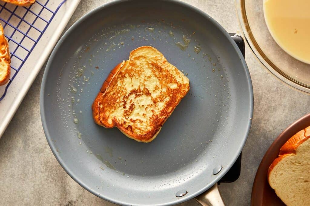 a top down shot of a pan with a brioche slice facing toasted side up cooking in the pan