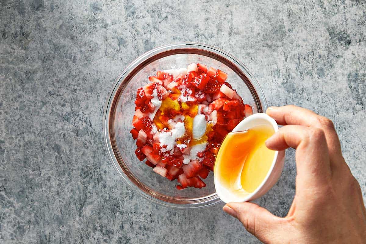 Top overview of finely chopped strawberries in a bowl being drizzled with honey and sugar.