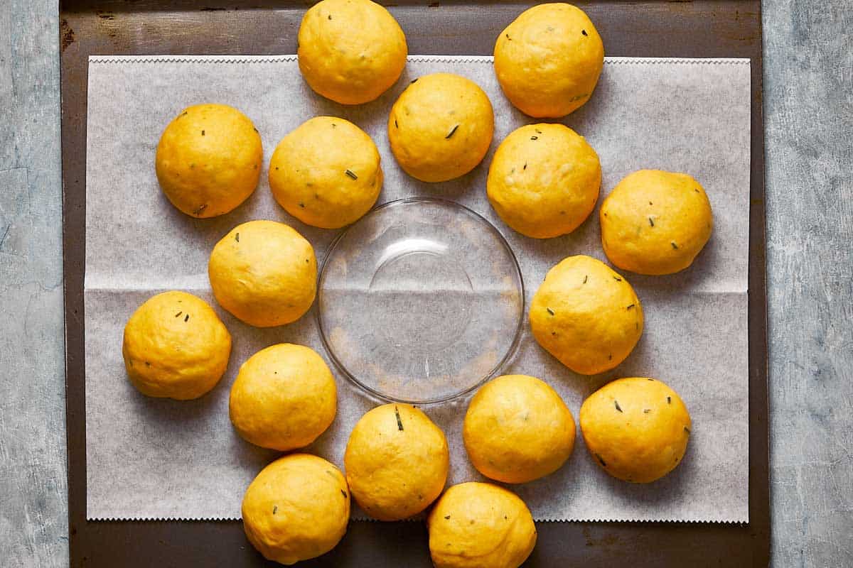 an oiled glass bowl upside down on a baking tray with small balls of bread dough around it