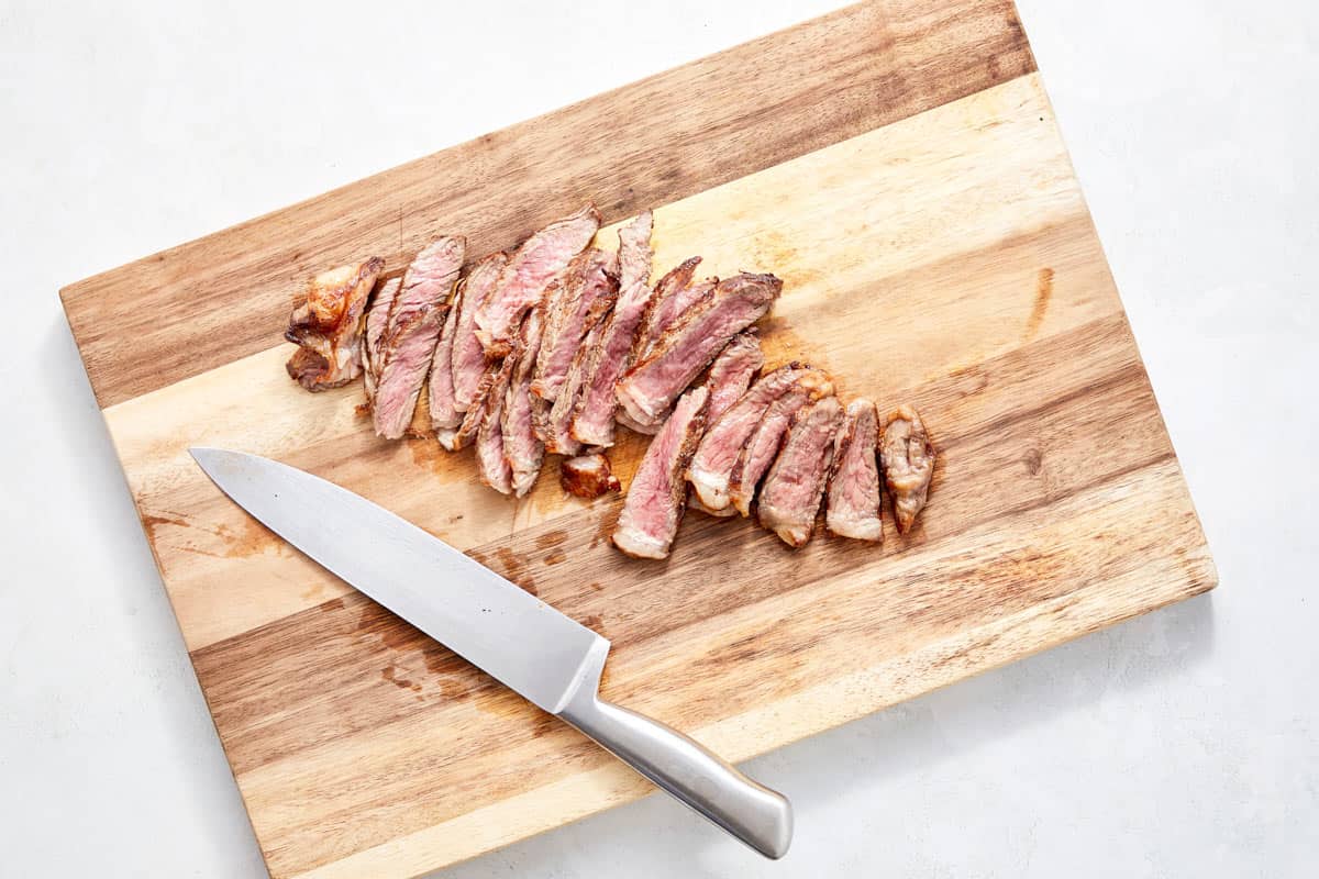 Steak sliced thinly against the grain on a board.