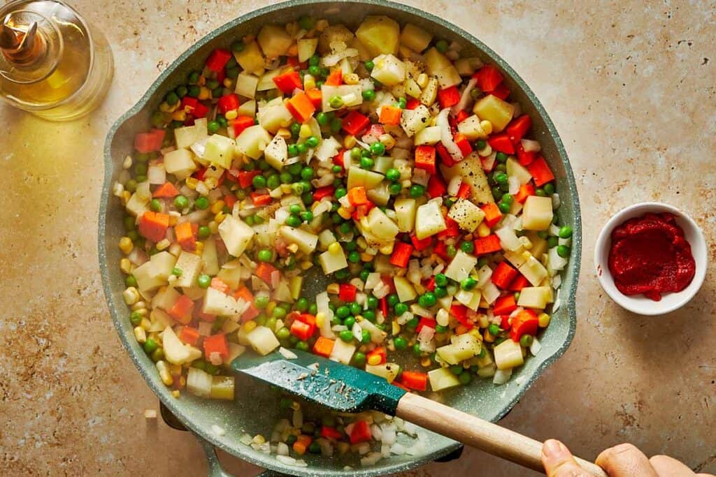 vibrantly colored vegetables chopped up into little cubs being mixed in a bowl with a wooden spoon