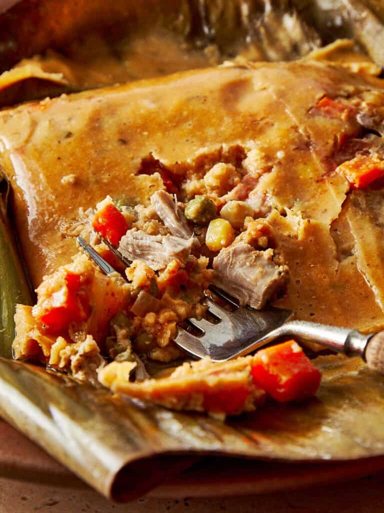Top-down view of a turquoise Dutch oven filled with stacked tamales wrapped in banana leaves