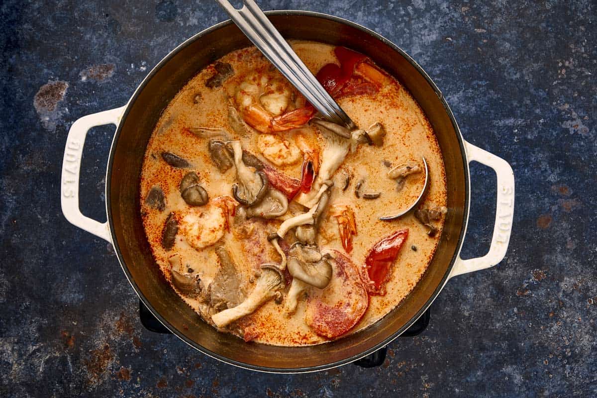 Pot of creamy Tom Yum Kha soup with shrimp, mushrooms, and tomatoes ready to serve.