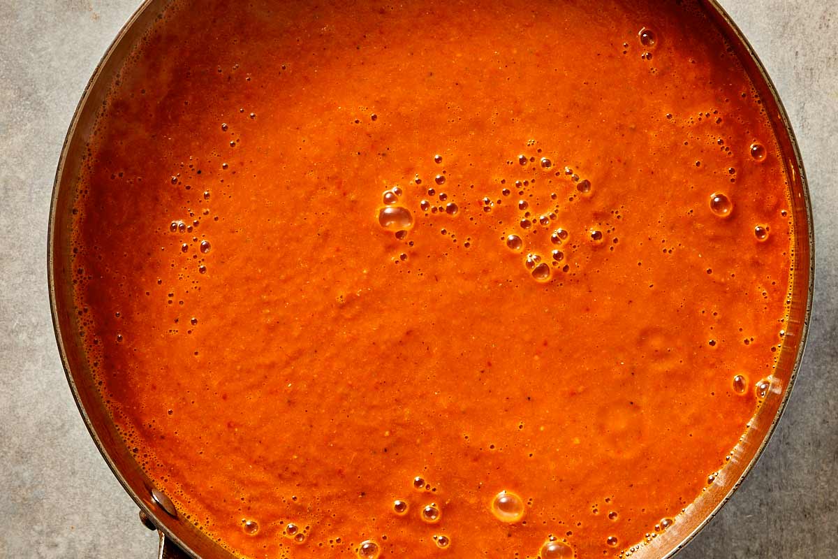Smooth blended tomato soup simmering in a pot, ready for the pasta to be added.