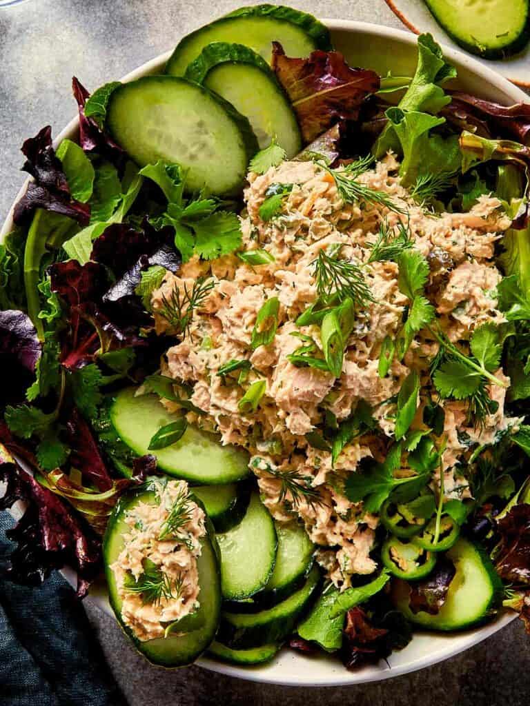 tuna salad for one served over mixed greens with sliced cucumber, fresh herbs, and jalapeño in a bowl
