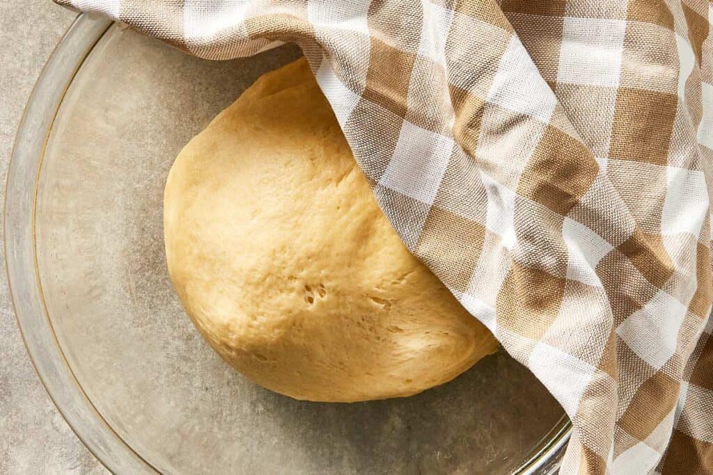 Dough resting in a bowl covered with a towel before rising