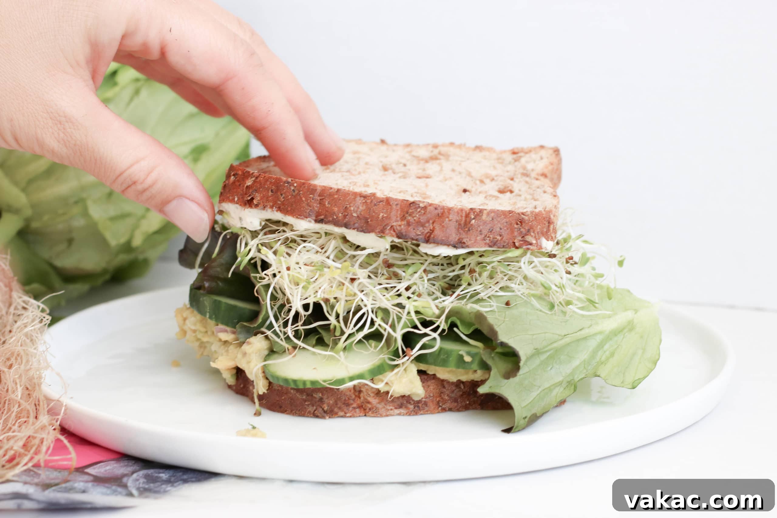 Power-Packed Green Goddess Chickpea Sandwich 3 Close-up of a cut Green Goddess Chickpea Salad Sandwich, showcasing the creamy chickpea mash, crisp lettuce, cucumber, and sprouts.