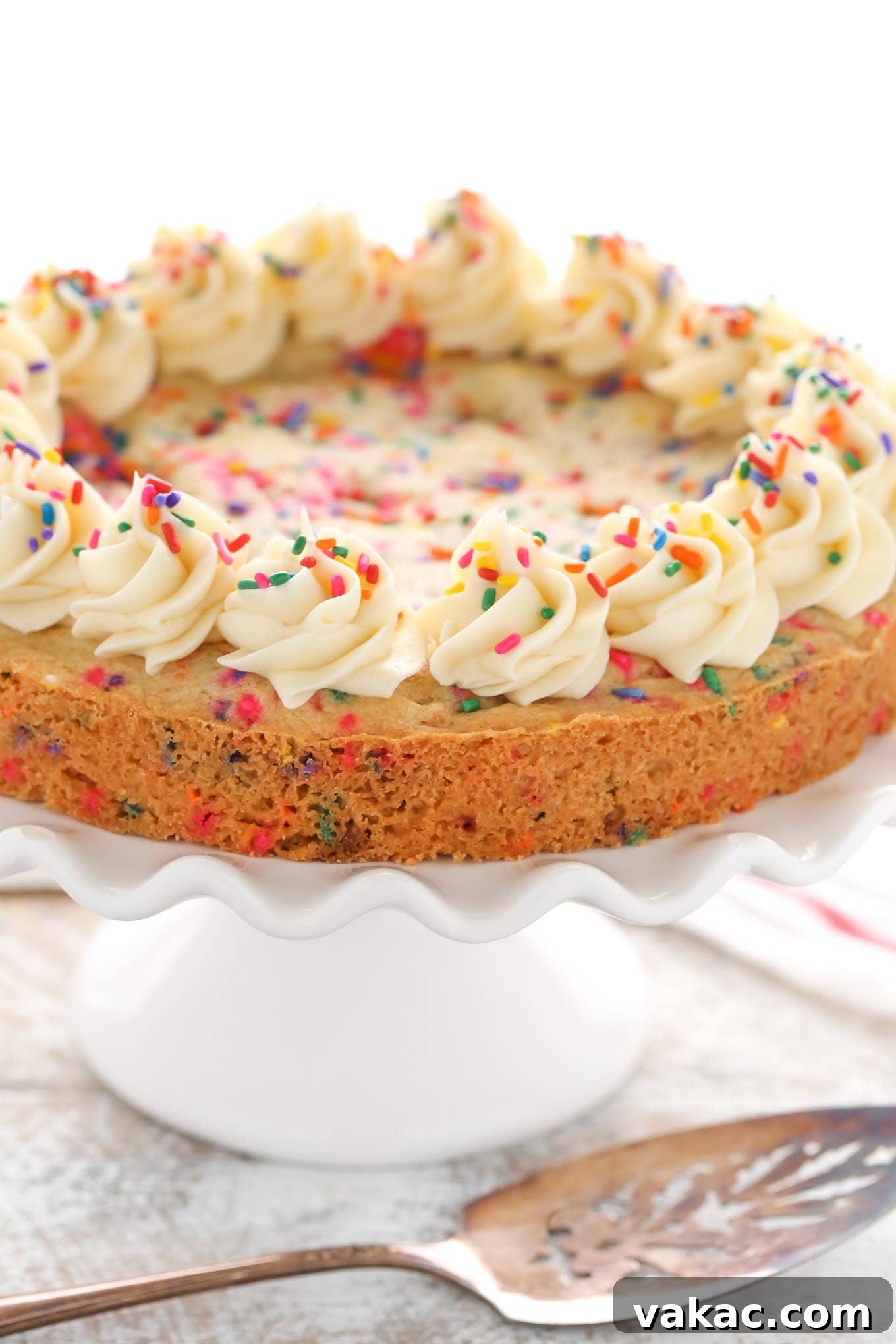 A sugar cookie cake topped with whirls of vanilla buttercream, seen from the side. 