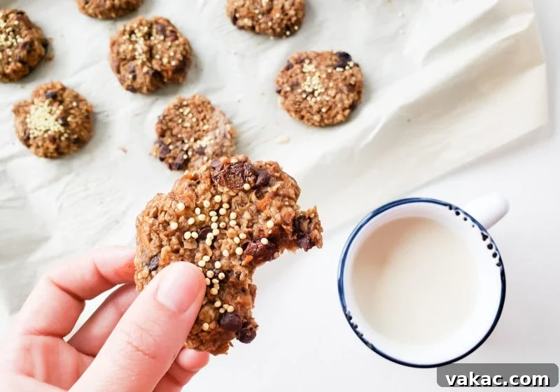 Make-Ahead Vegan Gluten-Free Carrot Cake Breakfast Cookies 5 Lindsay Pleskot, a registered dietitian, smiling and holding a carrot cake breakfast cookie. Beside her, a white mug with a blue rim is filled with milk, and more breakfast cookies are visible on a baking sheet, creating a warm and inviting scene.