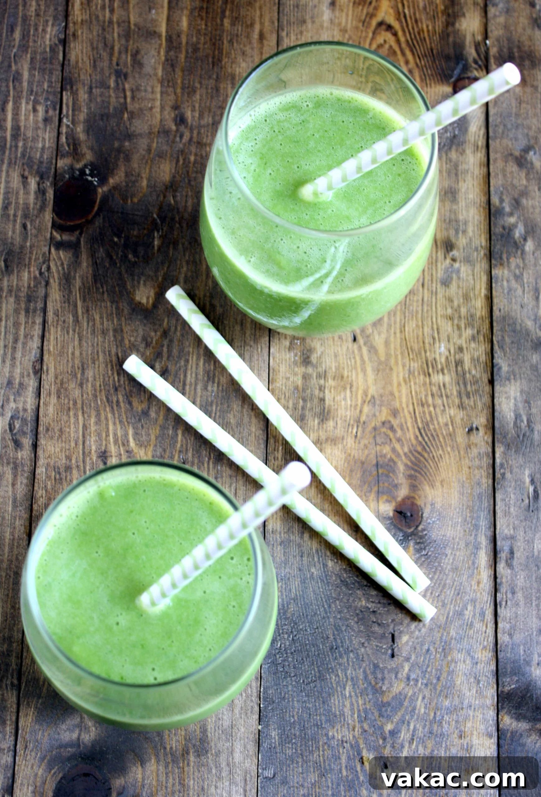 Rejuvenating Green Cleanse 3 Overhead view of two spinach banana pineapple smoothies with straws, showcasing their vibrant green color.