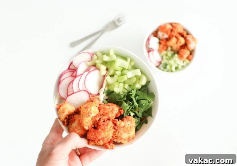 Lindsay Pleskot, RD holding a white bowl with baked buffalo cauliflower, greens, celery, and watermelon radish over a white surface.