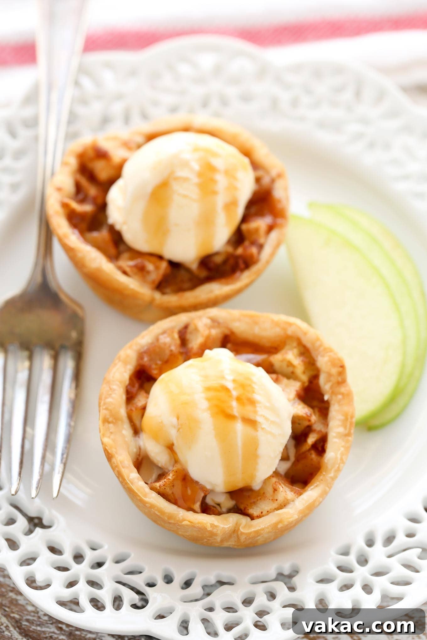 Sweet Apple Pie Bites 11 Two mini apple pies topped with a small scoop of ice cream and a drizzle of salted caramel sauce. A fork and a few slices of apples lay on the plate next to the pies.