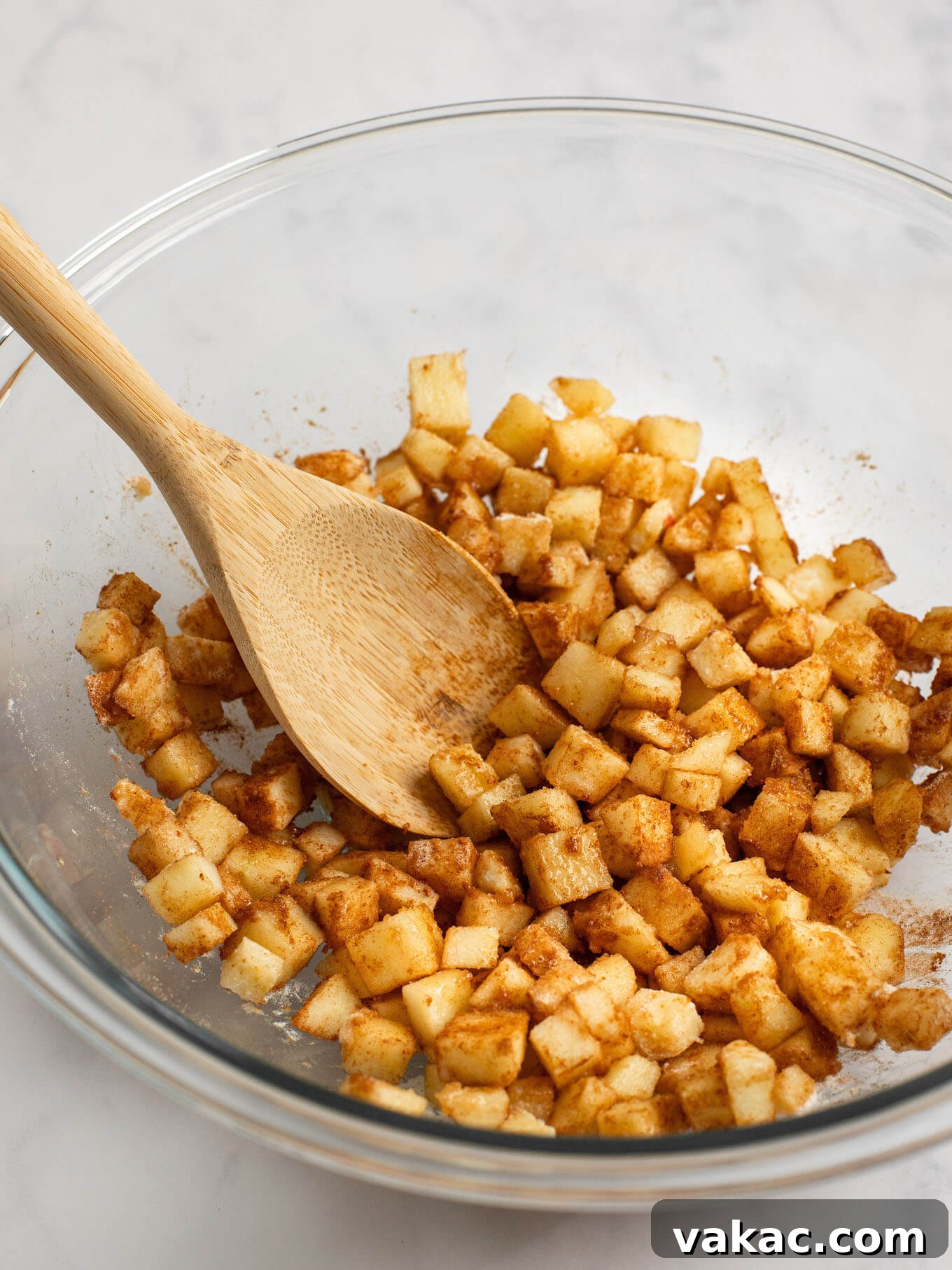 Sweet Apple Pie Bites 6 Apple pie filling mixed together in a glass mixing bowl with a wooden spoon.