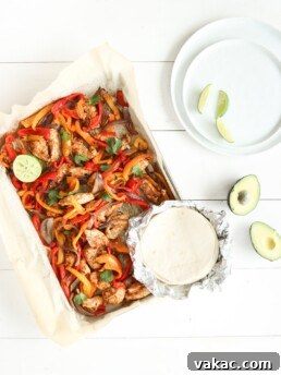 30 minute sheet pan fajitas made with simple ingredients like bell peppers, red onion, and chicken on a sheet pan over a white surface with soft shell tacos and avocados beside it.