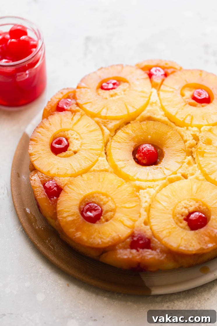 A finished pineapple upside down cake resting on a plate with a jar of cherries in the background.