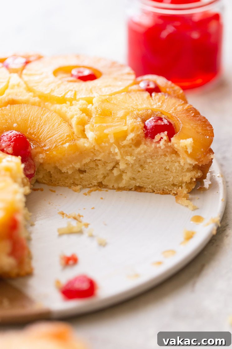 A pineapple upside down cake on a plate with one slice taken out to show the texture of the cake.