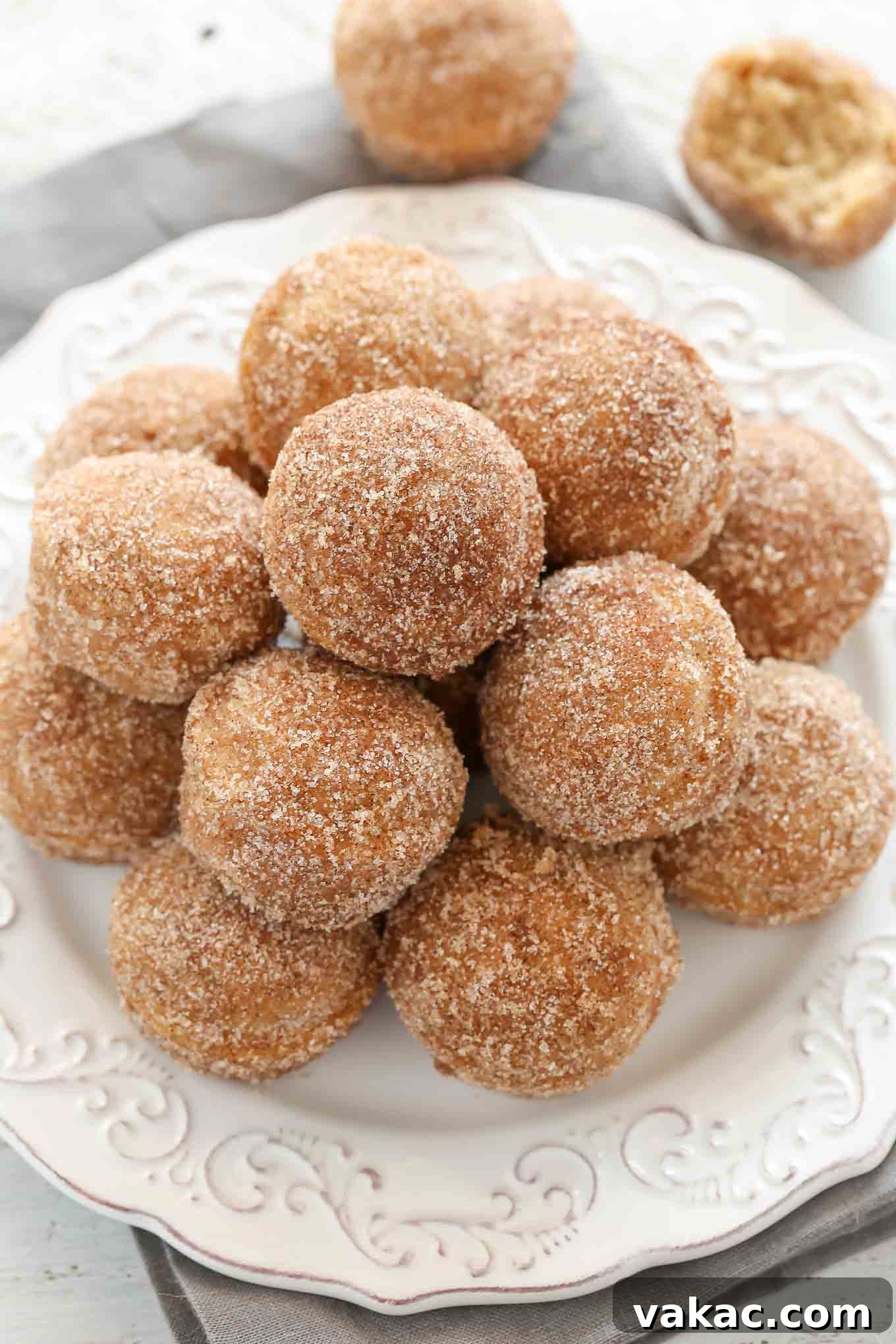 Baked Apple Cider Donut Bites 4 Overhead view of a white plate piled high with golden-brown apple cinnamon donut holes, dusted generously with cinnamon sugar.