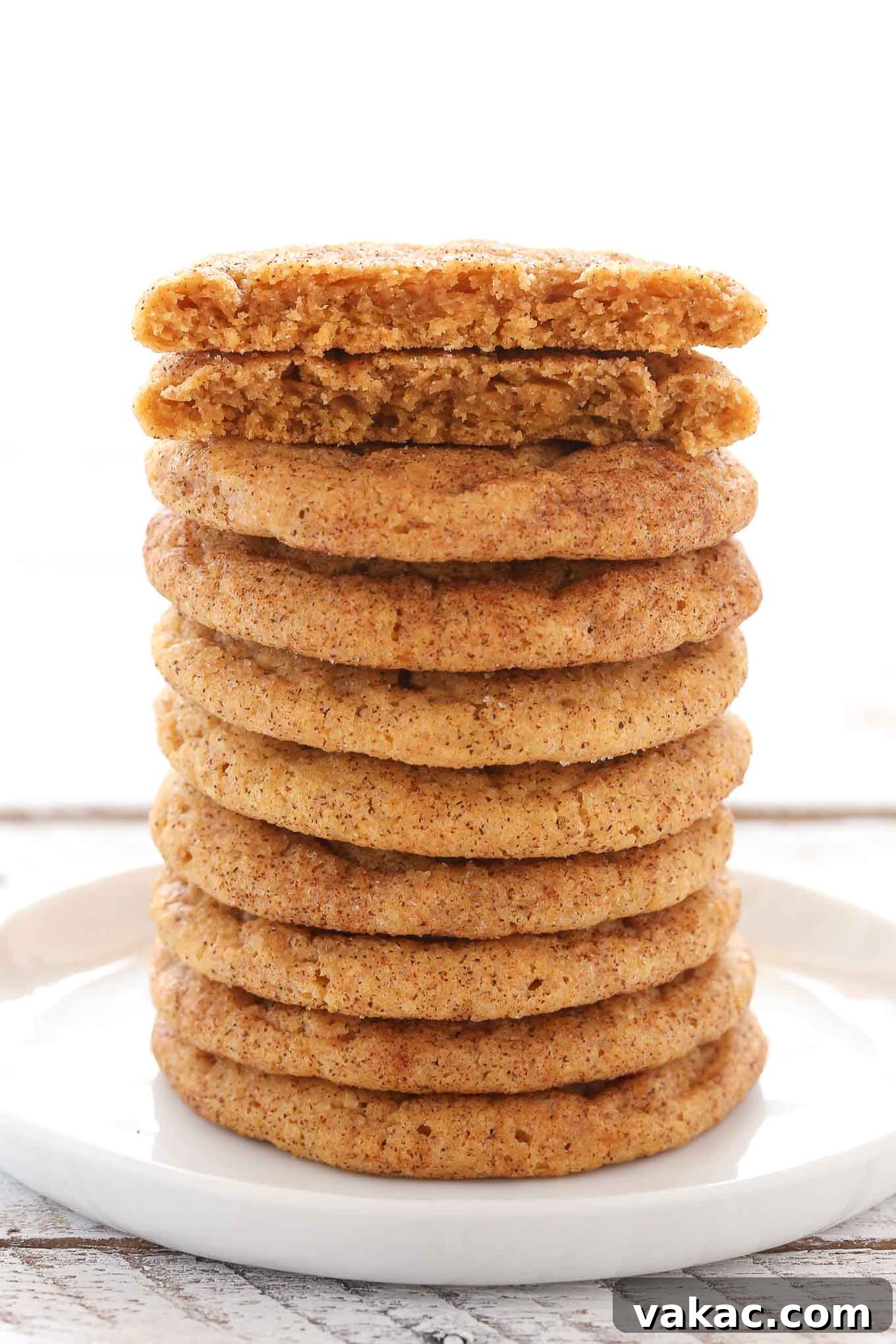 Spiced Pumpkin Snickerdoodles 11 A tall, tempting stack of pumpkin snickerdoodles on a white plate, with the top cookie broken in half to reveal its soft, chewy interior.
