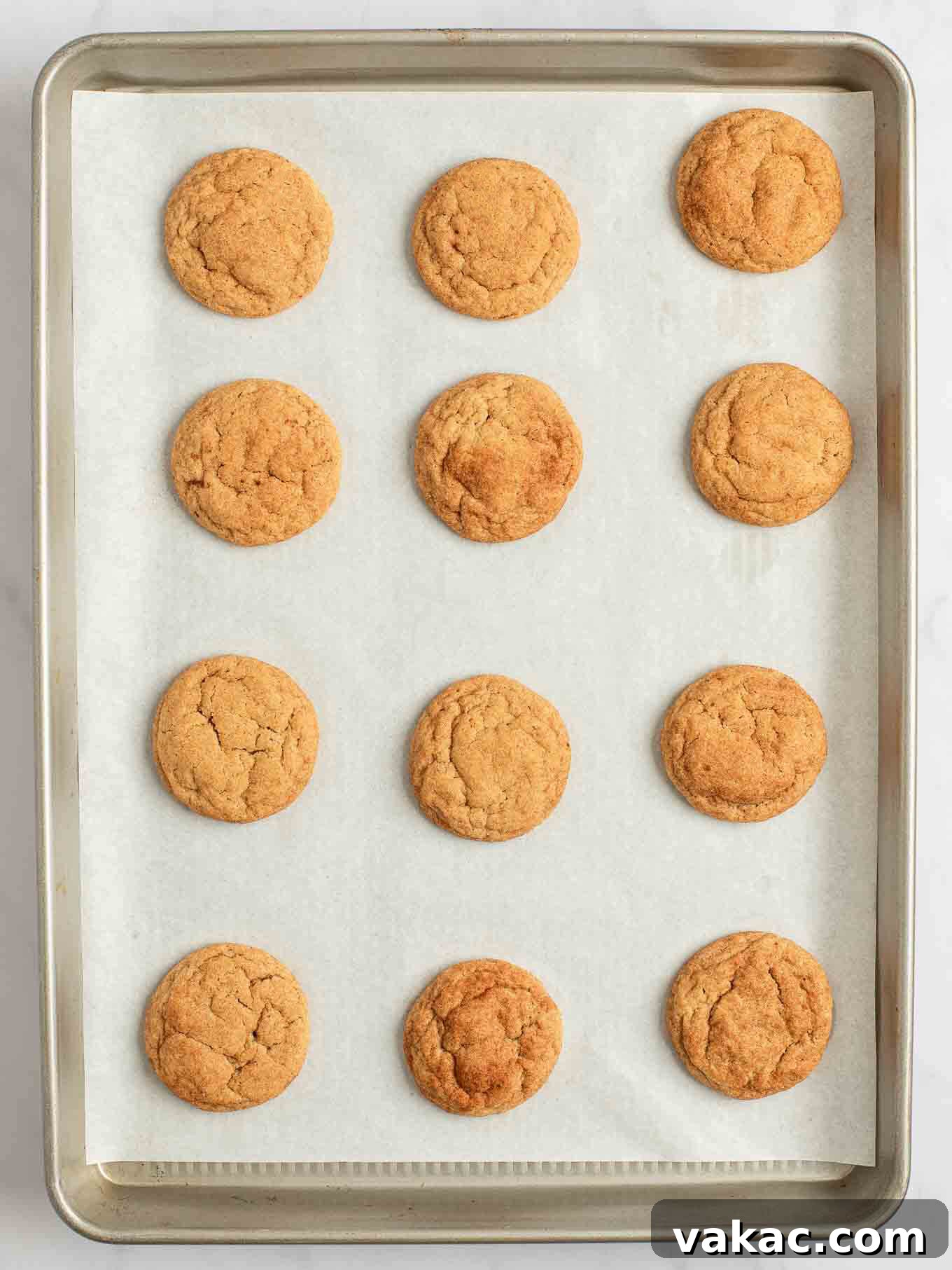 Spiced Pumpkin Snickerdoodles 9 An overhead shot of perfectly baked pumpkin snickerdoodles cooling on a baking sheet lined with parchment paper, their crinkled tops dusted with cinnamon sugar.
