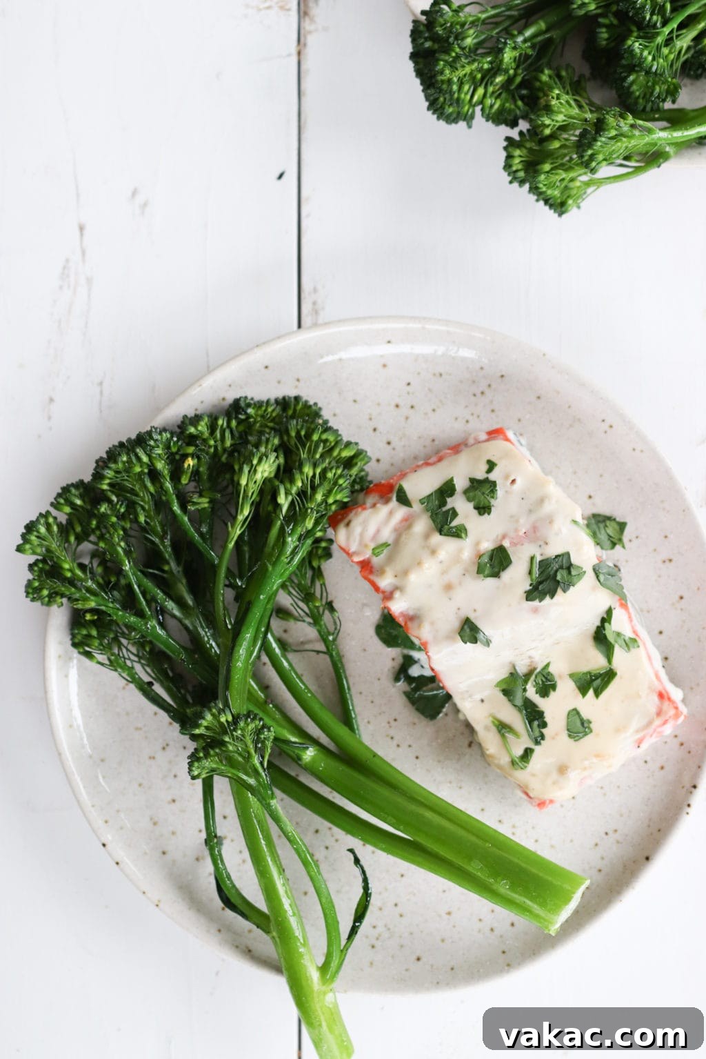Oven-baked Miso Yogurt Salmon Recipe by Lindsay Pleskot, Dietitian A perfectly baked Miso-Yogurt Salmon fillet on a plate, garnished with fresh herbs and served alongside vibrant green broccolini. The golden-brown crust of the salmon suggests a delectable texture, highlighting the simplicity and appeal of this easy oven-baked dish.